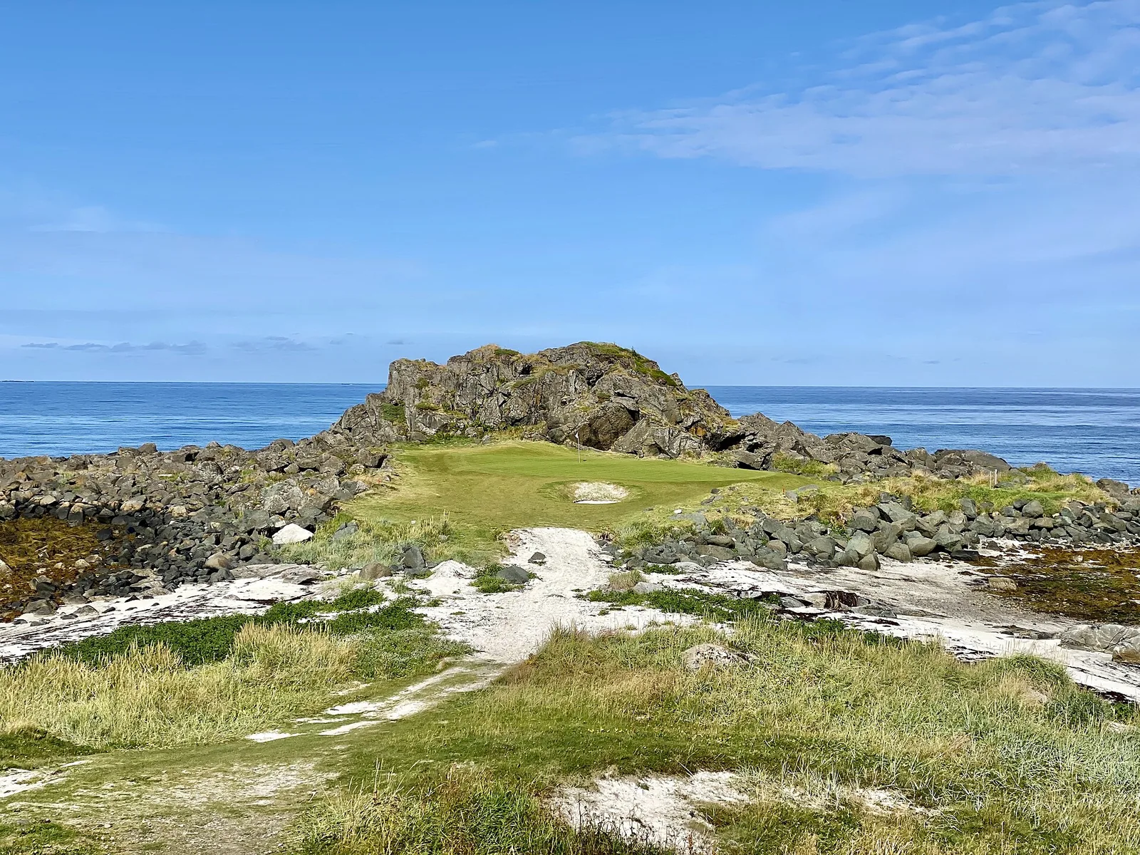 A links green sits on a rocky spit with the Norwegian Sea and mountains behind it, lit low by the midnight sun.